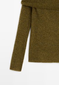 Manche et torse partiel d'un pull en maille duveteuse vert olive avec une manche longue ajustée et un ourlet côtelé sur fond blanc.