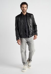 Schwarze Lederjacke mit Stehkragen, Reißverschlusstaschen; kombiniert mit grauen Jeans und modischen Sneakers. Glatte Textur und taillierte Passform.