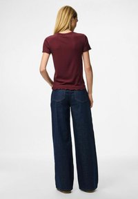 Burgundy räfflad kortärmad topp med vågig kant, i kombination med vida mörkblå jeans. Tyget verkar mjukt och texturerat.