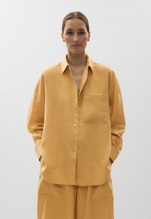Chemise en lin jaune à boutons avec une coupe décontractée, poche poitrine unique et une texture lisse. Présente un col classique et des détails de boutons.