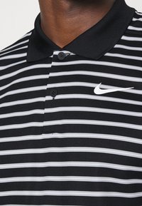 Black and white striped polo shirt with a classic collar, three buttons, and a white Nike logo on the chest. Made of textured fabric.