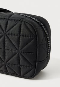 Borsa cosmetica nera trapuntata con motivo triangolare, chiusura con zip e accessori in argento, e texture di tessuto liscia. Forma rettangolare compatta.