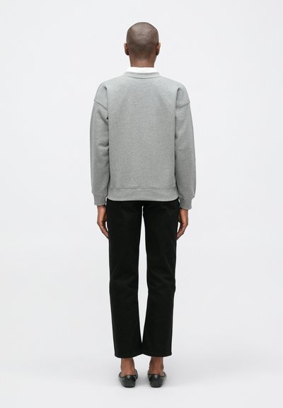Sudadera gris con cuello redondeado, hombros caídos y puños acanalados, combinada con pantalones negros de pierna recta y bailarinas negras.