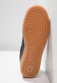 Černá podrážka tenisek s kruhovými a liniovými vzory. Tělově hnědá gumová podešev zajišťuje přilnavost a odolnost. Na boku je viditelné logo Nike.