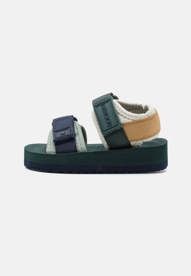 Sandală cu talpă texturată verde, superior din material textil cu curele albastre și aurii, cataramă reglabilă și suport căptușit pentru gleznă.
