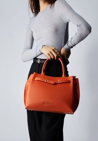 Sac à main en cuir orange avec une finition texturée, deux poignées supérieures et une fermeture à clip. Exposé sur un fond neutre.