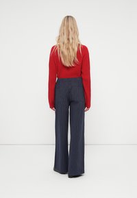 Pull rouge côtelé à manches longues associé à un pantalon large rayé bleu marine. Texture lisse, avec des poches au dos du pantalon.