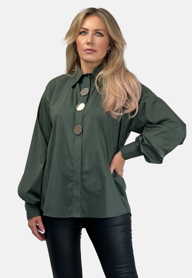 Ciemnozielona koszula zapinana na guziki o luźnym kroju, z oversize'owymi rękawami i trzema dużymi srebrnymi guzikami z przodu. Gładki, lekki materiał.