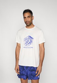 Άσπρο αθλητικό μπλουζάκι με μπλε γραφικό βουνού και κείμενο "ASICS FUJITRAIL", συνδυασμένο με μπλε σορτς με σχέδια.