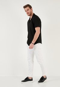 Rövid ujjú fekete gombos ing, laza szabással, fehér slim-fit nadrággal párosítva, és fekete cipővel, tépőzárral.