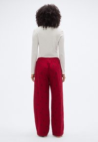Pantalon rouge à jambes larges avec une taille élastique, présentant un motif floral noir subtil. Le tissu semble doux et légèrement texturé.