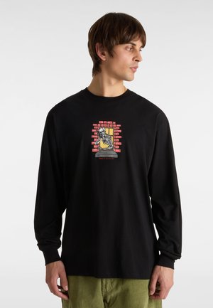 Sort langærmet t-shirt med et centralt grafisk motiv af et skelet bag et vindue, prydet med røde mursten og gule accenter.
