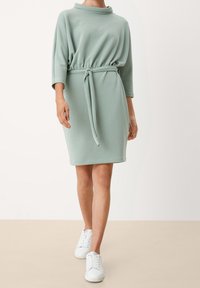 Vaaleanvihreä, polvipituinen mekko, jossa on korkea kaulus, joustava vyötärö ja solmittava vyö. Kangas on sileä; yhdistetty valkoisiin tennareihin.