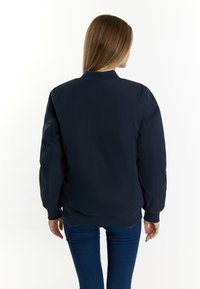 Marine bomberjack met ribbelkraag en -manchetten, met een gladde, matte afwerking en een ontspannen pasvorm. Zichtbare naden op de schouders en rug.