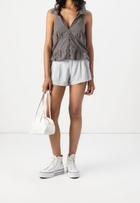 Černobílé kostkované bezrukávové tričko s volánkovým lemem, spárované se šedými pruhovanými šortkami. Bílá kabelka a tenisky na vysoké podrážce dotvářejí celý vzhled.