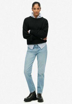 Black knit sweater, blue and white striped shirt underneath, light blue jeans, and black lace-up boots. Textured fabric and relaxed fit.