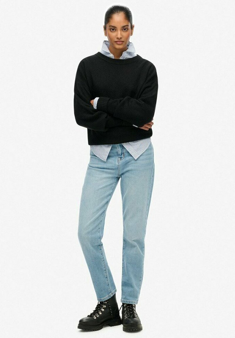 Black knit sweater, blue and white striped shirt underneath, light blue jeans, and black lace-up boots. Textured fabric and relaxed fit.