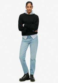 Zwarte trui met brede halslijn, gedragen over een blauw gestreept hemd, gecombineerd met lichtblauwe spijkerbroek en zwarte veterlaarzen.