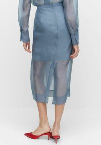 Ljusblå, halvgennomsiktig midiklänning med slits bak, midjeband och en slät textur, kombinerad med röda spetsiga klackskor.