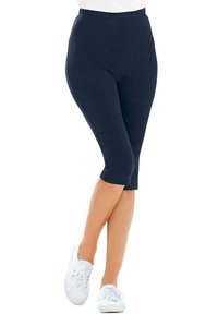 Donkerblauwe knielange legging gemaakt van zachte stof, met een elastische tailleband en een gladde textuur, gecombineerd met witte sneakers.