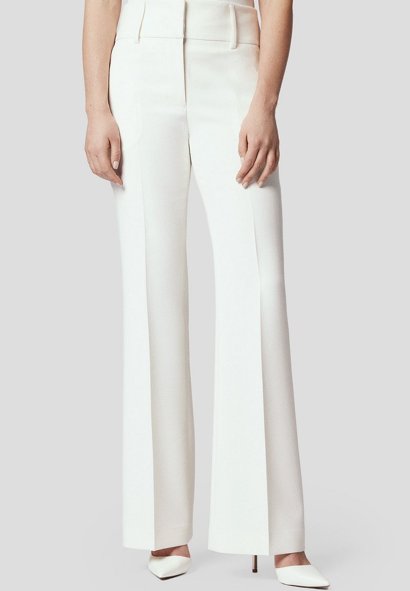Białe, wysokogatunkowe, szerokie spodnie o wysokim stanie, wykonane z gładkiego materiału, z wyraźnymi liniami i subtelnymi bocznymi kieszeniami. Zestawione z szpilkami o spiczastym nosku.