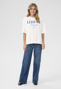 White oversized t-shirt with blue "LEISURE League" print, paired with blue wide-leg jeans. Black shoes, smooth texture and relaxed fit.