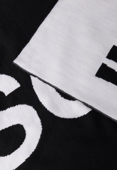 Ασπρόμαυρο ύφασμα με έντονα, μερικώς ορατά μεγάλα γράμματα και μια διπλωμένη ενότητα που δείχνει διαφορετικά τμήματα κειμένου.