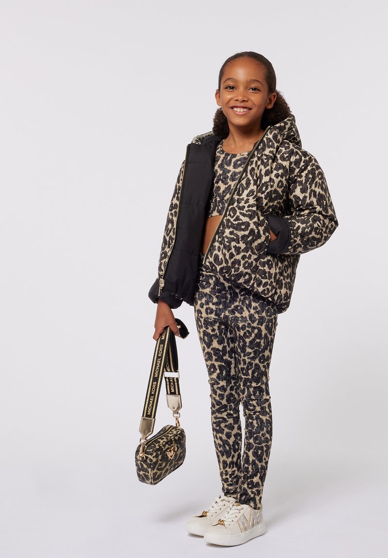 Gilet noir rembourré sur un crop top à motif léopard et un legging, associé à des baskets blanches et un petit sac à motif léopard avec une bandoulière.