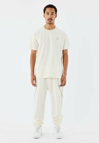 T-shirt corto color avorio con un logo grigio sottile e cuciture laterali a contrasto abbinato a joggers avorio con tasche.