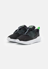 Black mesh athletic shoes with green accents, featuring a textured rubber sole and elastic laces for secure fit. Modern design elements included.
