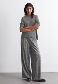 Pulover tricotat gri cu mâneci scurte, asortat cu pantaloni evazați în carouri în nuanțe de gri. Pantofi negri completează ținuta. Textură netedă.