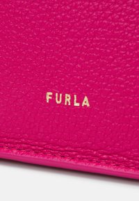 Furla bőr anyag élénk rózsaszínben, textúrált felülettel. Arany, dombornyomott logóval rendelkezik, amely kiemeli a jellegzetes kézműves munkát.