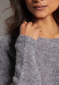 Grauer gestrickter Pullover mit lockerer Passform, der eine gerippte Textur und dezenten Glanz aufweist. Die Ärmelbündchen sind etwas oversized und betonen das gemütliche Design.