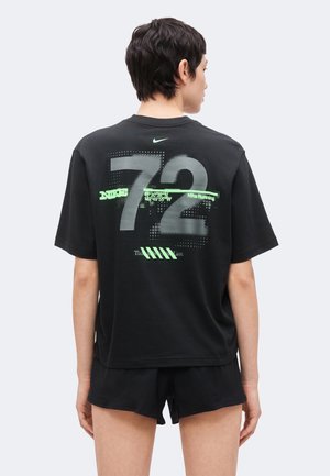 Personne vue de dos portant un t-shirt Nike noir avec un grand numéro gris 72 et un texte vert, associé à un short noir.