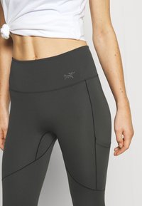 Leggings taille haute de couleur gris foncé, confectionnés dans un tissu extensible. Dotés d'une poche latérale et d'un logo discret au niveau de la taille.