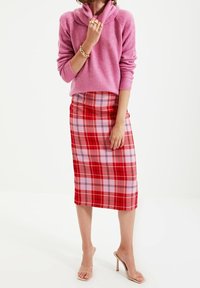 Rosa, stickad tröja med cowl-hals; röd rutig midi kjol med olika nyanser av rosa och röda rutor; genomskinliga klackskor.