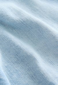 Lyseblå denimstof med en glat tekstur, der har et klassisk twillvævemønster. Overfladen viser minimal falmning og en ensartet farve.