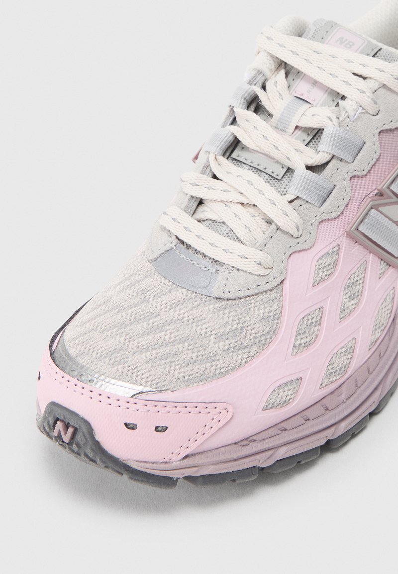 Baskets de sport gris clair avec des accents roses, dessus en maille texturée et détails réfléchissants. Comprend de larges lacets et une semelle en caoutchouc durable.
