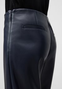 Zbliżenie na osobę noszącą granatowe, wysokie skórzane spodnie z tylną kieszenią i bocznym zamkiem, w połączeniu z czarną górą.