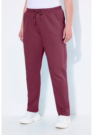 Bordeauxfarbene Sweatpants aus Baumwollmischung, mit elastischem Bund und Kordelzug, seitlichen Taschen und schmal zulaufenden Beinen. Dazu werden weiße Sneaker getragen.
