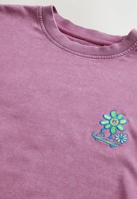 Lila Baumwoll-T-Shirt mit gestickten Blumen in Blau, Grün und Gelb. Klassischer Rundhalsausschnitt und weicher, strukturierter Stoff.