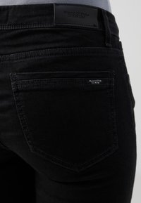 Svarta denimjeans har en slank design med en bakficka och en läderlogotyp vid midjan. Tyget har en mjuk textur.