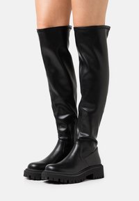 Svarta knähöga stövlar i mjukt syntetläder med en kraftig gummisula och sidodragkedja för enkel på-och-avtagning.