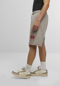 Lys grå shorts med røde grafiske detaljer og elastisk talje, parret med beige og creme sneakers samt hvide ankelstrømper.