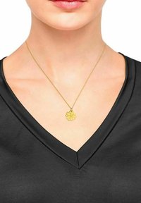 Collana d'oro con un pendente a forma di fiore, appesa a una delicata catena, indossata sopra una maglietta nera a V. Texture liscia, design semplice.