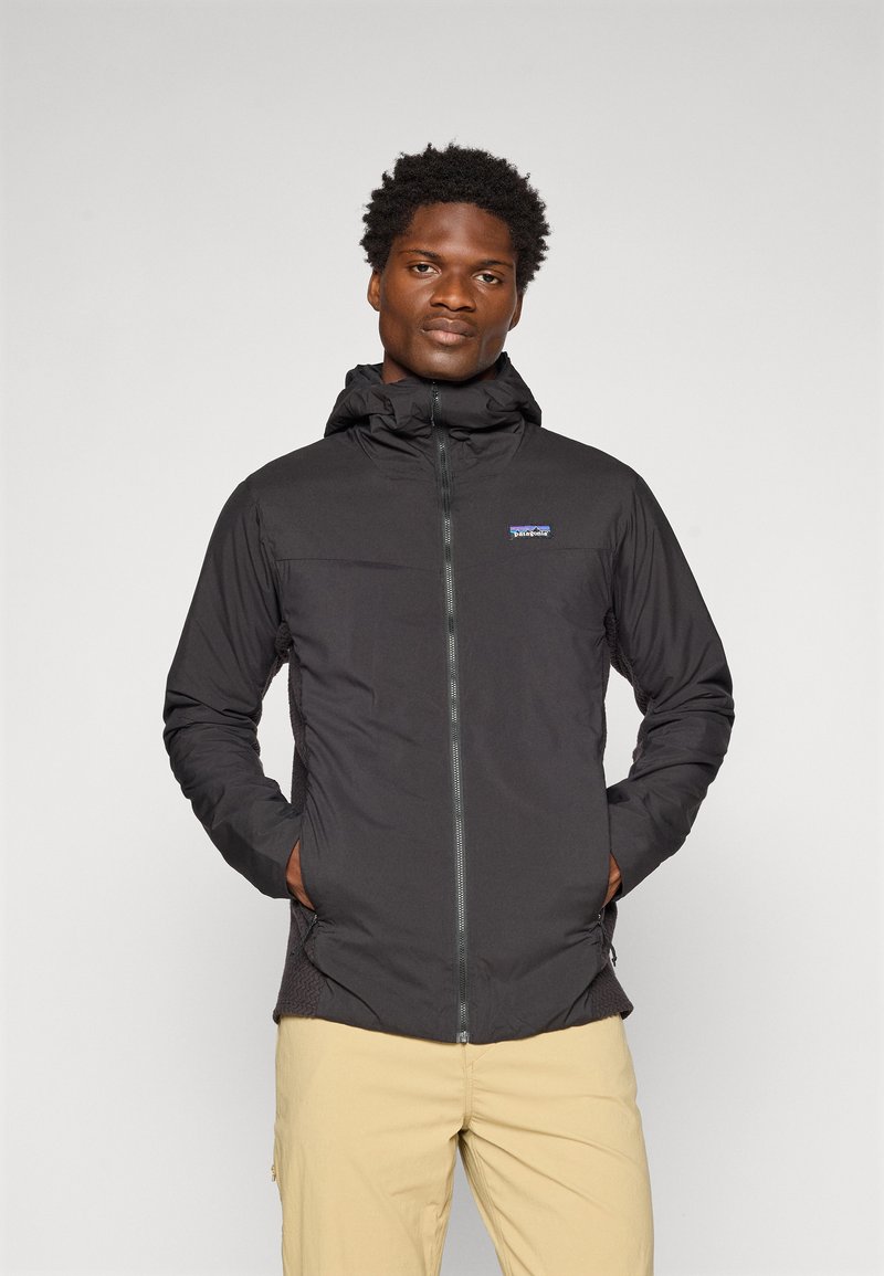 Veste zippée noire avec capuche, en tissu léger, poches latérales et poignets élastiques. Elle présente un petit logo sur la poitrine et des côtés texturés.