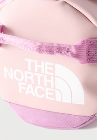 Približni posnetek roza torbe The North Face z ročajem iz blaga in belim logotipom na sprednji plošči.