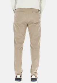 Pantaloni in cotone beige con polsini elasticizzati, due tasche posteriori e vestibilità rilassata. Abbinati a sneakers scure con suola bianca.