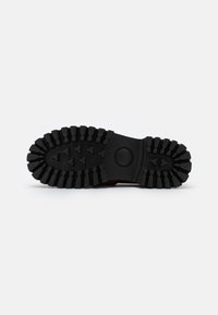 Semelle de chaussure en caoutchouc noir avec un profil profond et un motif pour traction, présentant une forme arrondie et des bords renforcés pour plus de durabilité.