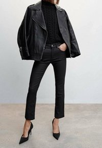 Černá kožená motorkářská bunda přes černý svetr z pleteniny s copánkovým vzorem, doplněná o úzké černé džíny a černé lodičky s špičatou špičkou.